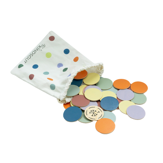 Draufsicht auf buntes Holzkonfetti in modernen Pastelltönen auf hellem Holztisch.