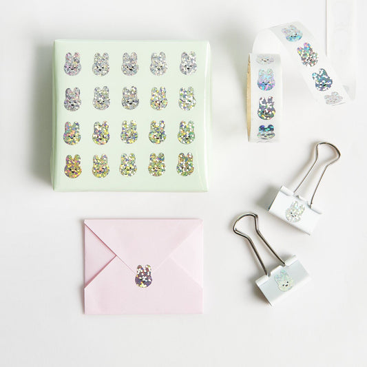 Weiße Papiertüte für Gastgeschenke, verziert mit glitzernden Hasen-Stickern als Verschluss